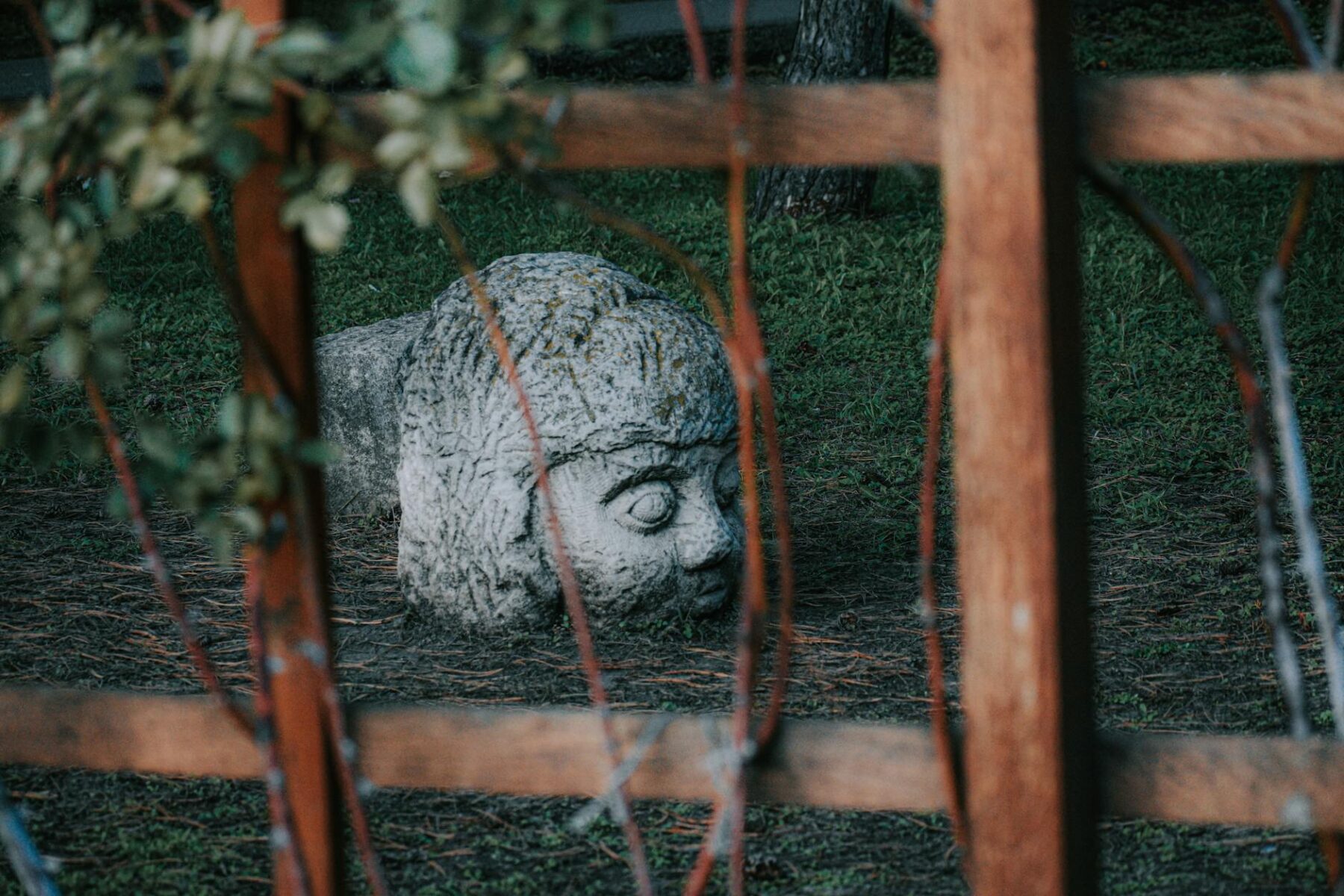 old stone human face statue on soil in garden
